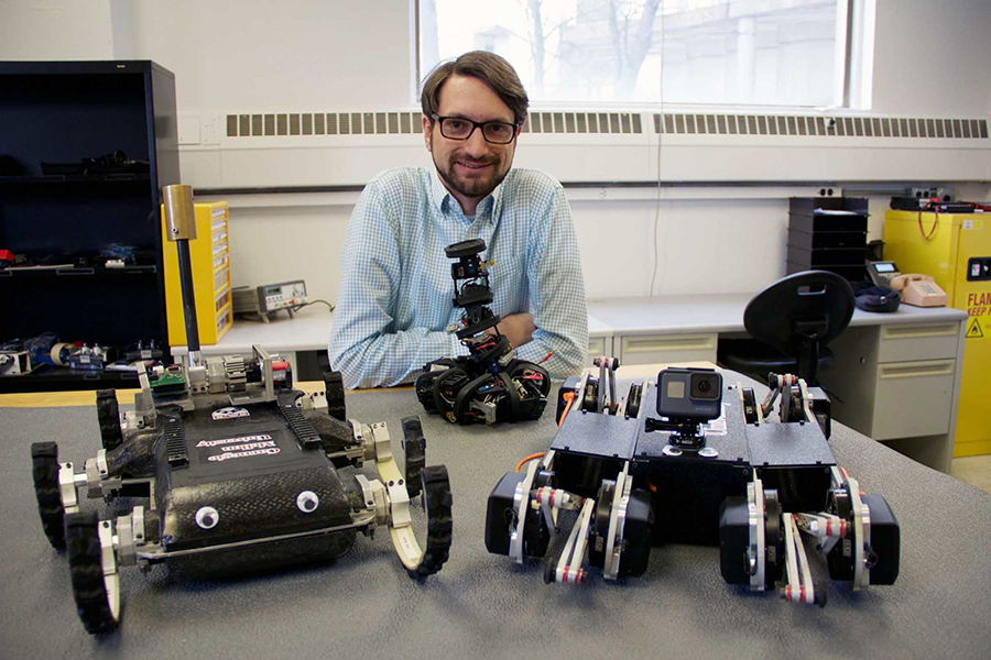 Aaron Johnson in his lab with multiple robots on the table in front of him